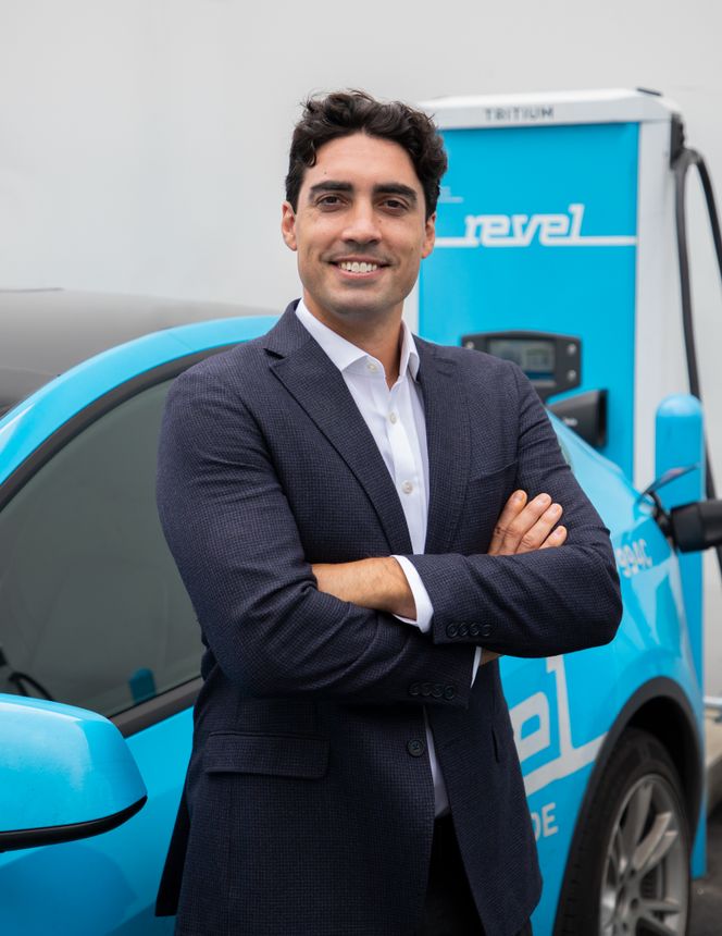 Headshot of a person standing with arms crossed in front of a vehicle